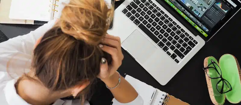 Overhead view of a stressed woman working at a desk with a laptop, phone, and notebooks.