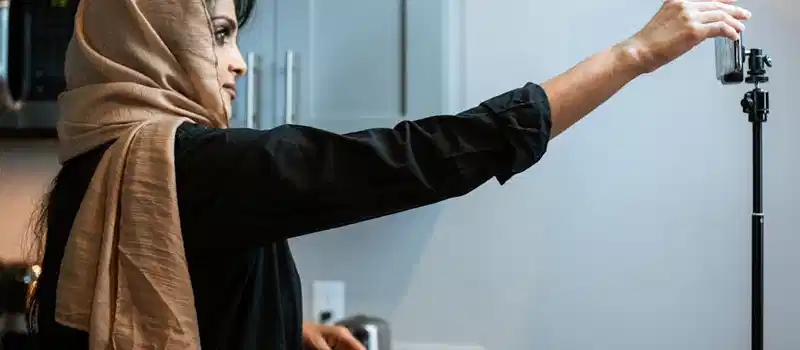 A Muslim woman in a hijab records a cooking video in her kitchen, focusing on her food presentation.