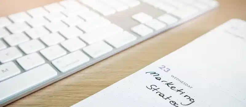 Notebook with marketing strategy note alongside a keyboard on a wooden desk.