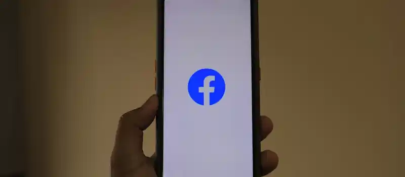 A smartphone held in hand showing the Facebook logo on its screen.