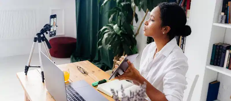 Black woman using electronic devices for vlogging indoors at home office.