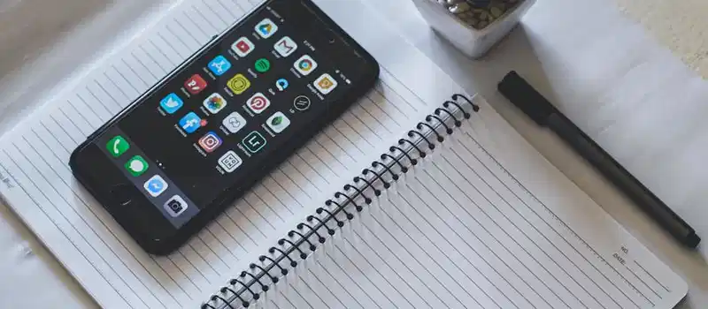 Flat lay featuring a smartphone on a spiral notebook beside a succulent plant and pen.
