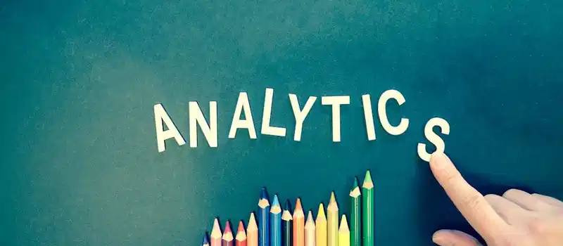 Colored pencils and letters spelling 'ANALYTICS' on a textured background with a hand.