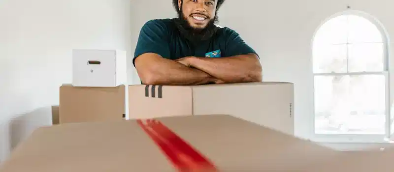 A cheerful mover standing with packed boxes indoors, ready for a moving day.