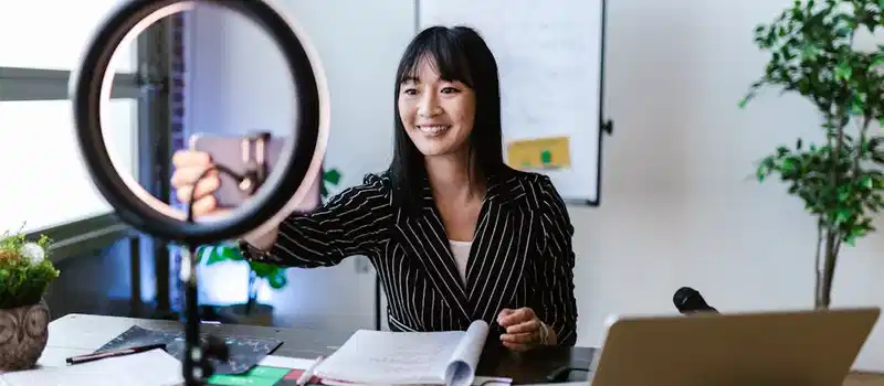 A woman vlogger uses her smartphone to create content in a professional office setting.