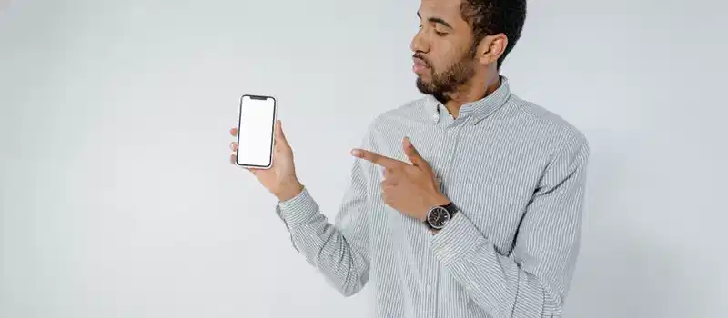 Confident man pointing at smartphone screen against a white background, showcasing technology.