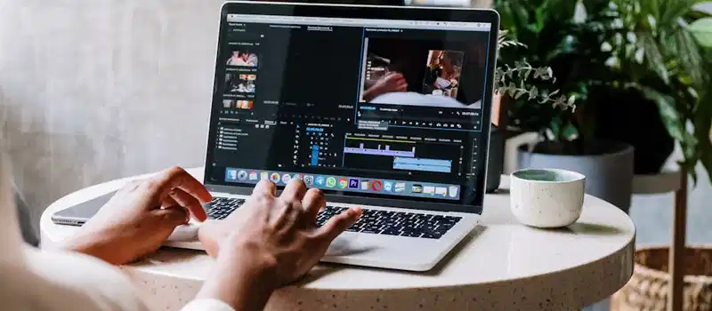 Freelance video editor working on a laptop in a cafe setting, utilizing Adobe software.