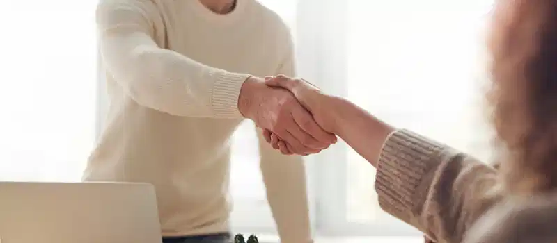 Close-up of professionals shaking hands over coffee in a modern office.