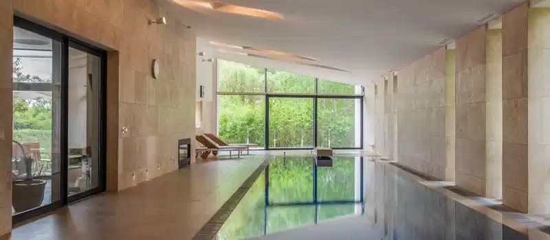 Deep swimming pool illuminated with lights in modern apartment with large windows in daytime