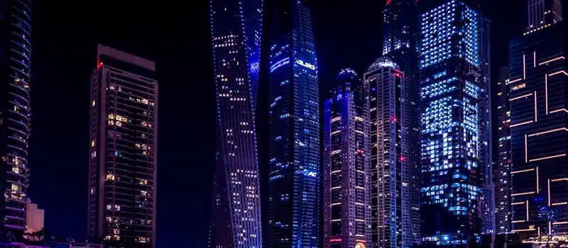 Illuminated skyscrapers of Dubai Marina at night, reflecting on the water.
