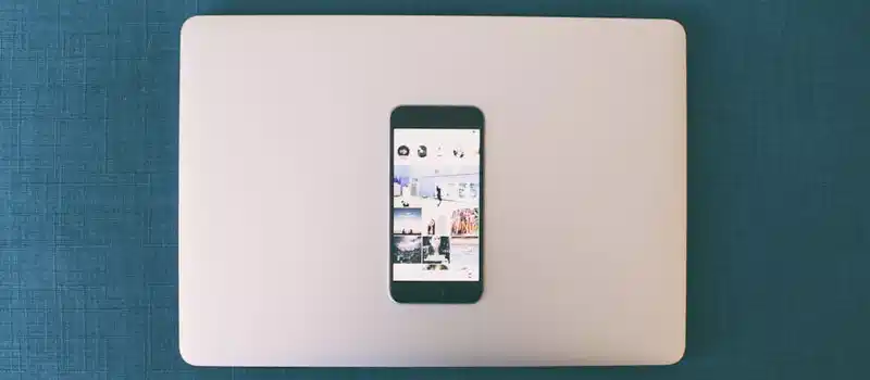 Flat lay of a smartphone on a laptop with social media photos on screen.