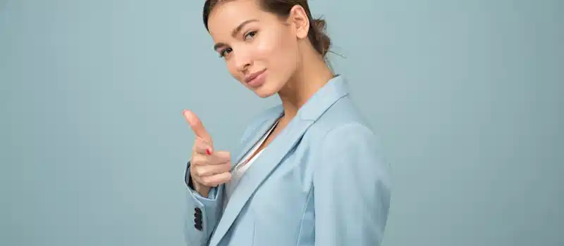 A young woman in a blue suit exhibits confidence with a relaxed pose against a blue background.