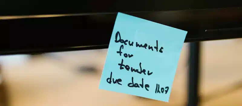 Close-up of a blue sticky note with a reminder attached to a computer monitor.