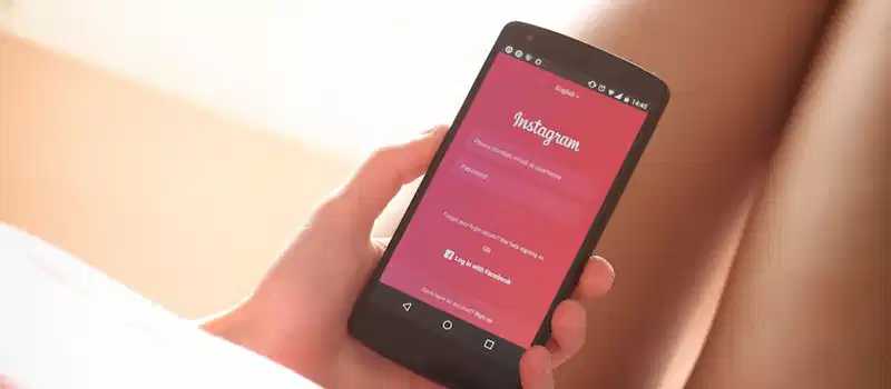 Woman holding a smartphone with Instagram login screen while relaxing indoors.