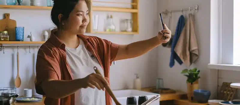 Woman cooking in kitchen and taking selfie, capturing the moment.