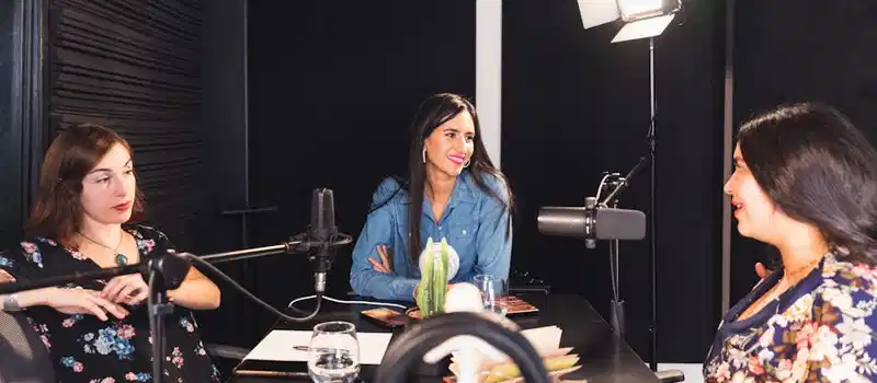 Three women engaged in a lively podcast discussion in a cozy indoor setting, fostering empowerment and connection.