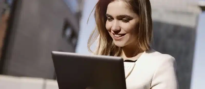 A woman joyfully using a digital tablet outdoors in the city during the day.