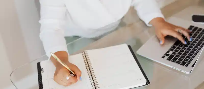 A person planning and typing on a laptop at a glass desk.