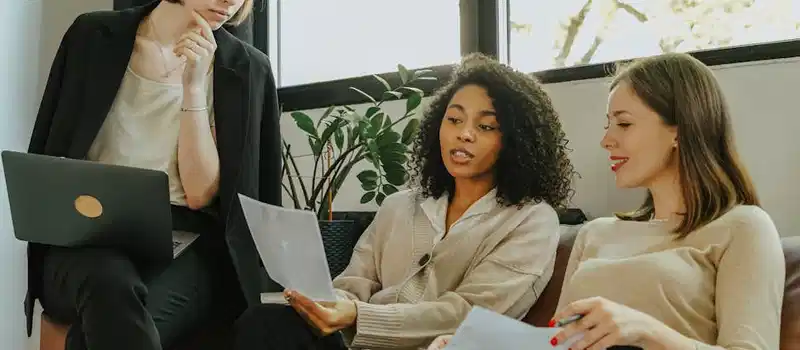 Three professional women engaged in a collaborative meeting in a modern office setting.