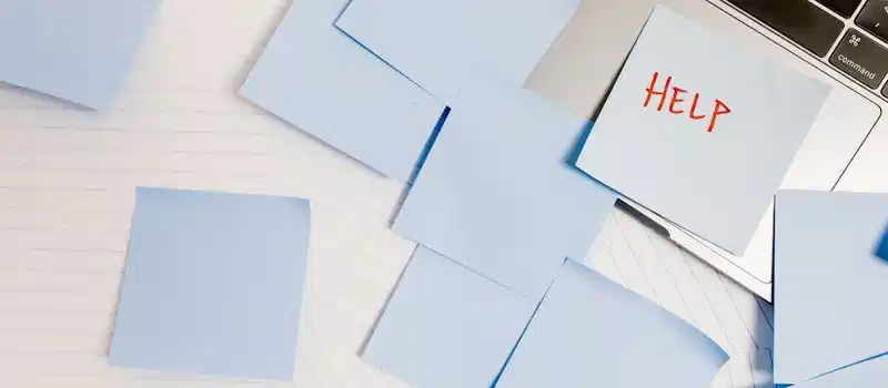 A cluttered workspace with sticky notes on a laptop, symbolizing overwhelm and need for help.
