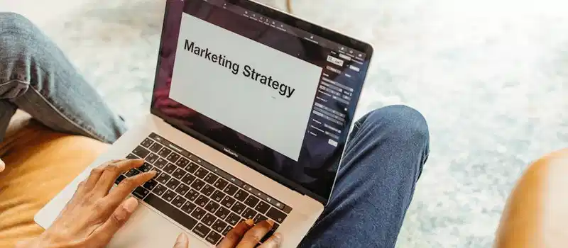 Close-up of hands using a laptop displaying a marketing strategy presentation indoors.