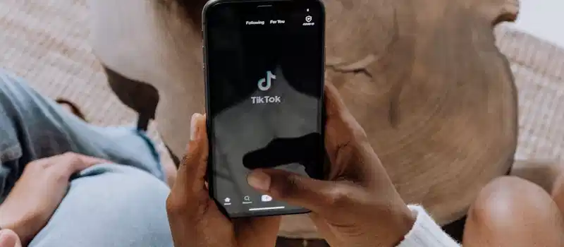Close-up of hands holding a smartphone displaying the TikTok app interface on a wooden surface.