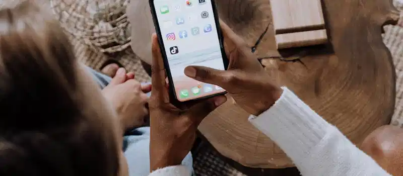 A person using a smartphone with social media apps, sitting at a wooden table. Perfect for tech lifestyle content.