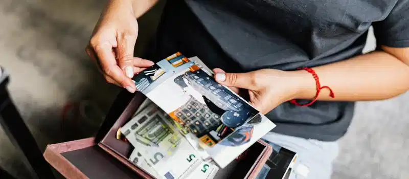 A woman holding photographs over a box with euro notes indoors.