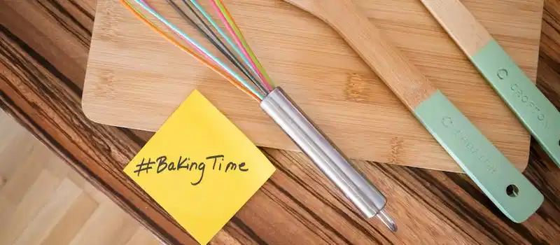 Top view of colorful kitchen utensils on a wooden board with a #BakingTime note.