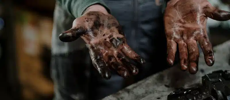 Close-up of a mechanic's dirty hands in a garage workspace with grease and spare parts.