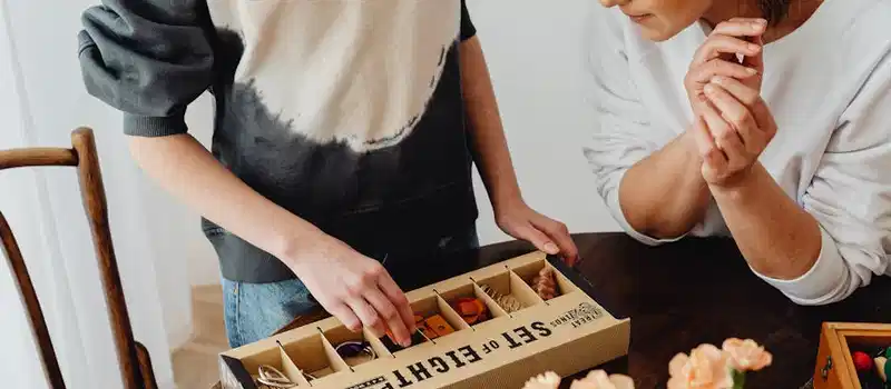 Two women enjoy a puzzle-solving activity with a boxed puzzle set indoors.