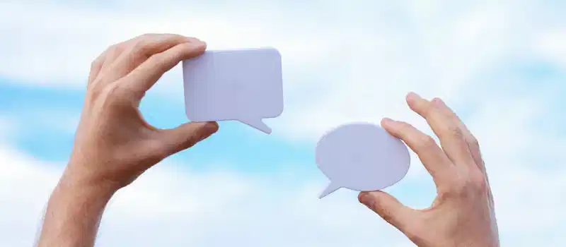 Close-up of hands holding speech bubbles, symbolizing communication and dialogue against a blue sky.