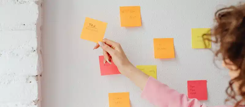 Woman organizing tasks using sticky notes on a wall, promoting productivity and planning.