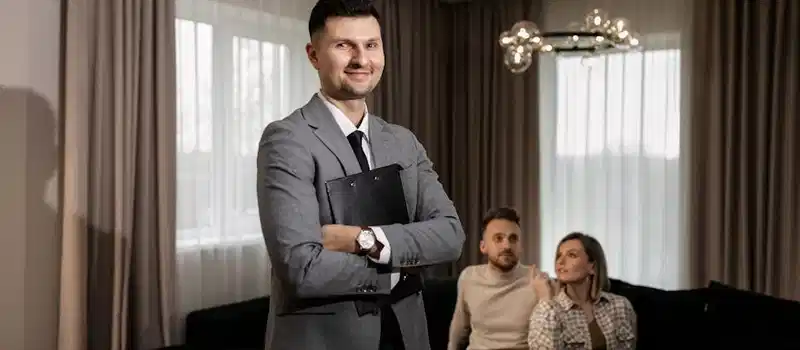 Smiling real estate agent with a clipboard indoors, showing a property to a couple.