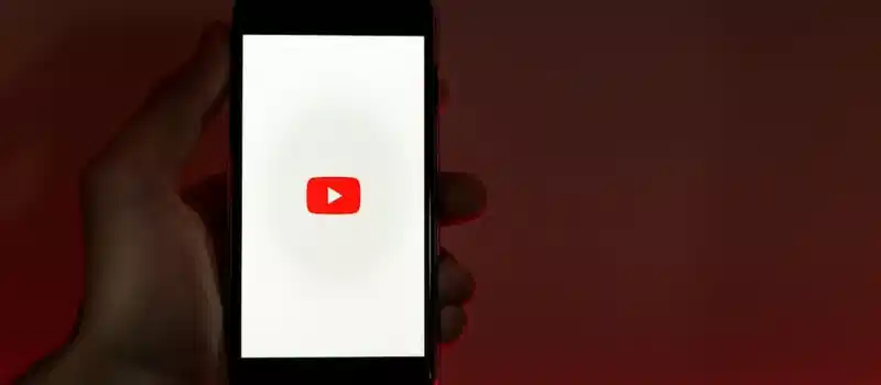 A hand holding a smartphone displaying the YouTube app against a red background.