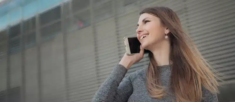 Woman in urban setting talking on phone, wearing casual attire, smiling.