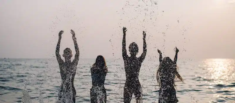 Silhouettes of four people joyfully splashing water in the sea during a beautiful sunset.