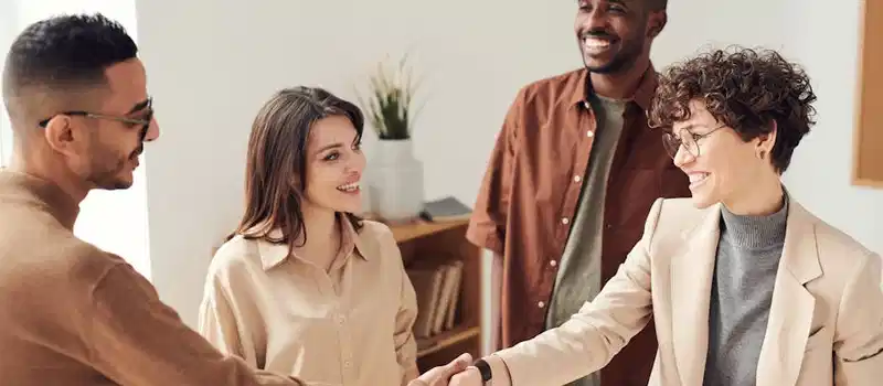 Four colleagues smiling and shaking hands in a bright office setting.