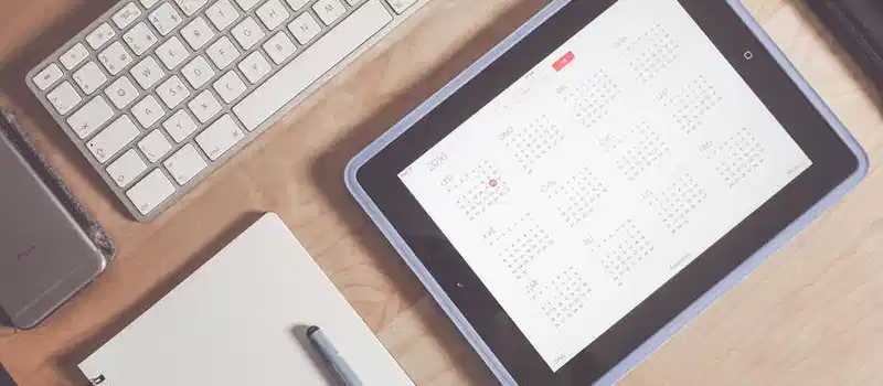 A tidy desk setup featuring a tablet displaying a calendar, keyboard, and stationary items.