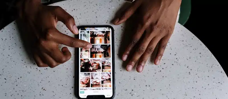 Hands interacting with smartphone displaying social media content on table in cafe setting.