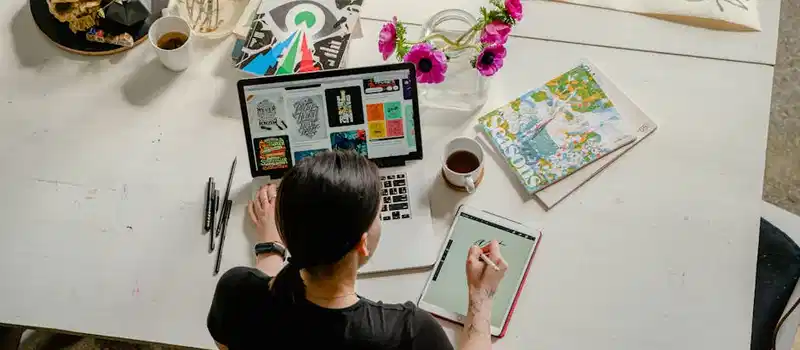 Artistic workspace featuring calligraphy and digital design on a tablet and laptop.