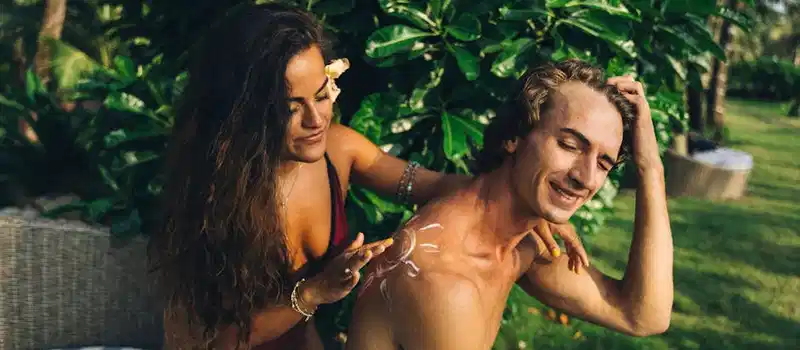 A couple applying sunscreen in a lush tropical setting, embracing summer leisure and skin care.