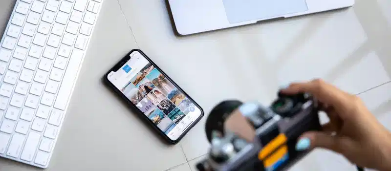 Person using vintage camera with smartphone and laptop in creative setup.