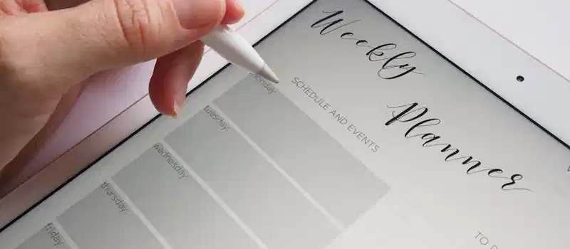 A stylus writing in a digital weekly planner on a tablet screen, ideal for organization.