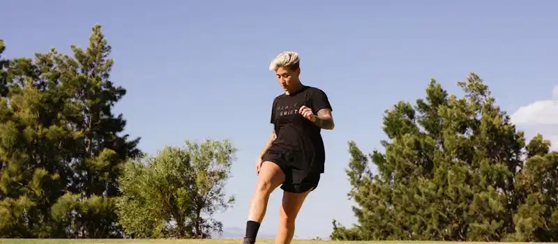A woman playing soccer on a grass field under a clear sky, showcasing energy and focus.