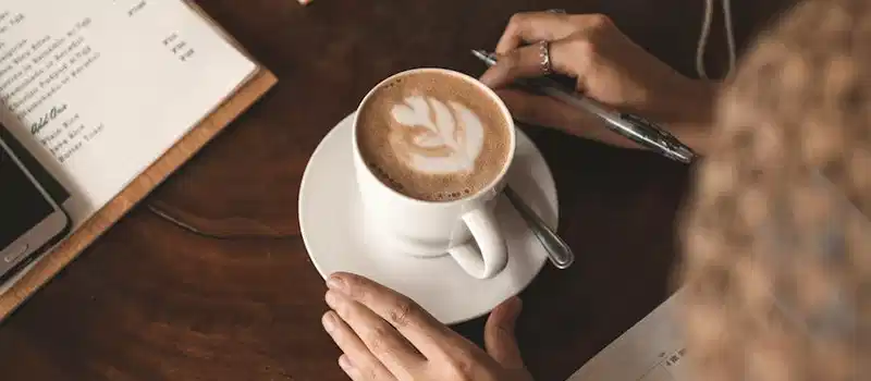 A woman enjoying a latte at a café while reviewing her planner. Warm and inviting.