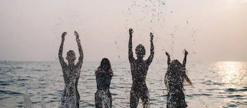 Silhouettes of four people joyfully splashing water in the sea during a beautiful sunset.