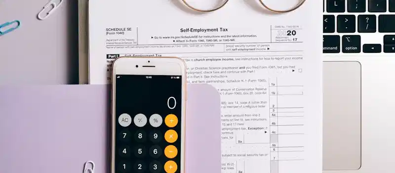 Flat lay of tax documents, smartphone calculator, and laptop for self-employment accounting.