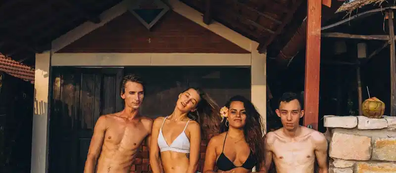 Four friends enjoying a sunny day at a rustic beachside hut, perfect for lifestyle ads.