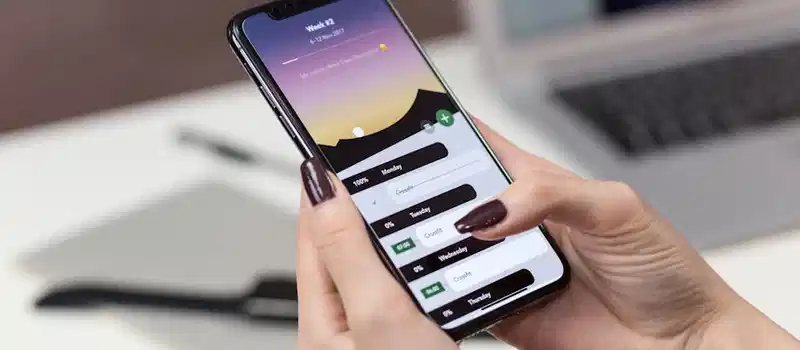 A woman interacts with a productivity app on her smartphone at a desk setup.